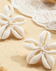 Pair of white shell earrings on a sandy surface with natural elements.