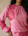 Woman wearing a pink dress with leaf pattern against a neutral background