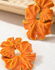 Pair of orange floral earrings on a textured beige surface