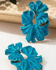 Pair of blue floral earrings on a beige surface