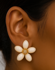 Close-up of an ear wearing a white flower-shaped earring with gold accents.