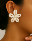 Close-up of a woman wearing a shell flower earring against a neutral background