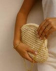 Person holding a woven clutch with a gold chain against a neutral background