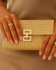 Person holding a gold clutch with a decorative clasp against a neutral background