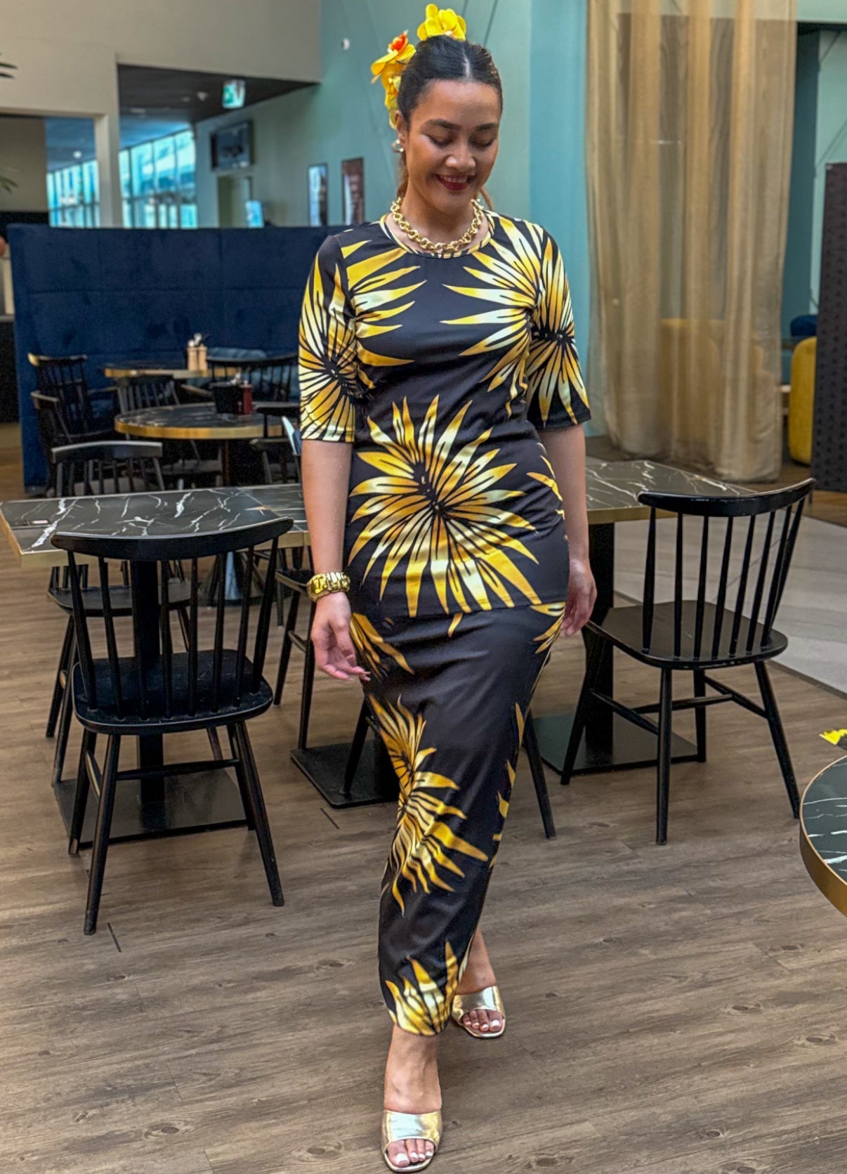Woman in a black and yellow patterned dress standing in a modern indoor setting.
