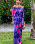 Woman wearing a purple floral dress standing outdoors with greenery in the background
