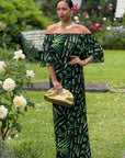 Woman in a green and black patterned dress standing in a garden with flowers.