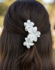 Person with long dark hair wearing a white floral hair clip outdoors.