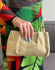 Person holding a beige clutch with a colorful dress in the background