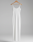 White slip dress hanging on a wooden hanger against a gray background