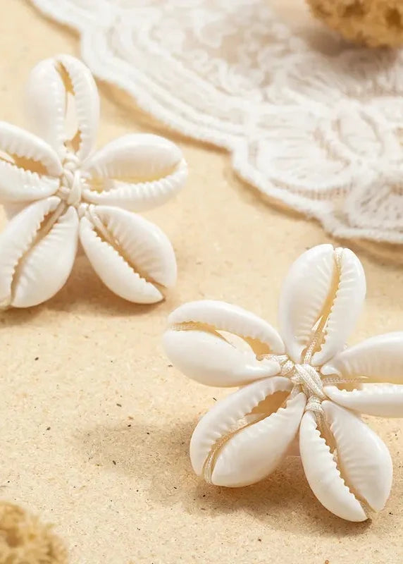 Pair of white shell earrings on a sandy surface with natural elements.