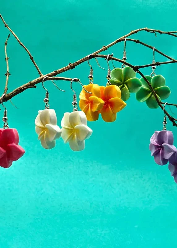 Colorful flower-shaped earrings hanging from a branch against a teal background