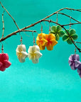 Colorful flower-shaped earrings hanging from a branch against a teal background
