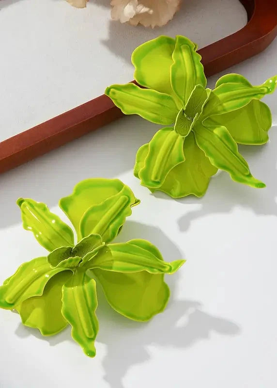 Pair of green flower-shaped earrings on a white surface with a wooden background.