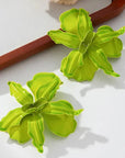 Pair of green flower-shaped earrings on a white surface with a wooden background.