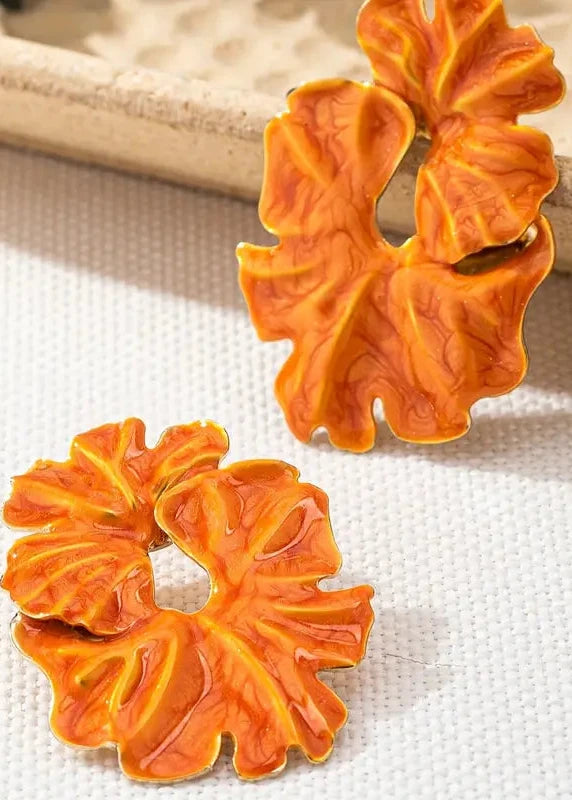 Pair of orange floral earrings on a textured beige surface