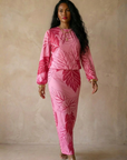 Woman wearing a pink outfit with leaf patterns against a beige background