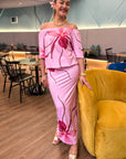 Woman in a pink floral off-shoulder top and skirt standing in a modern interior setting.