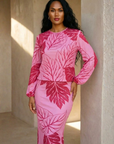 Woman wearing a pink outfit with leaf patterns standing against a beige wall.