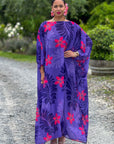 Woman wearing a purple dress with pink floral patterns standing outdoors.