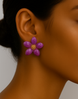 Close-up of a person wearing a purple flower-shaped earring against a neutral background