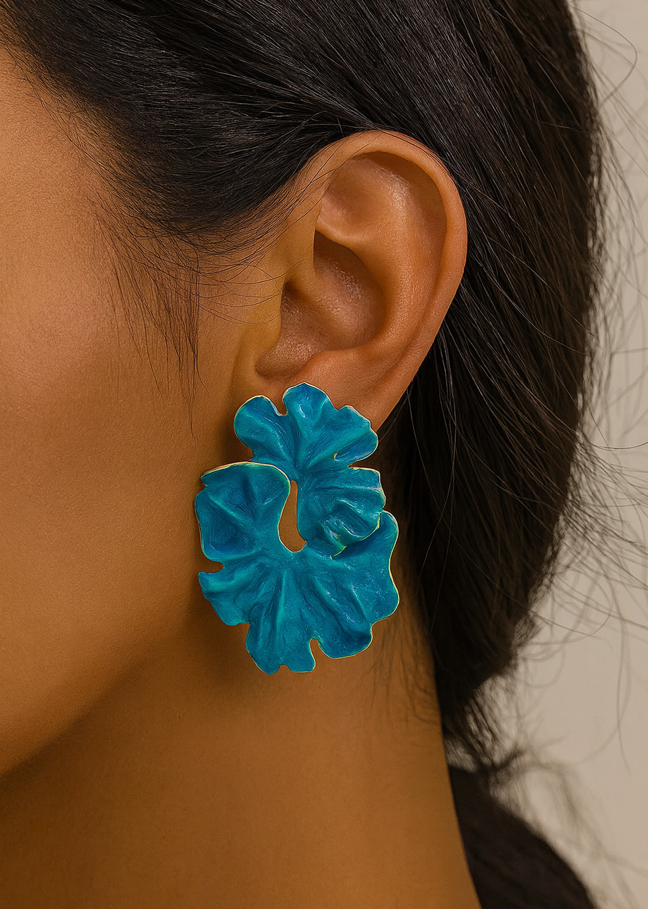 Close-up of a person wearing a blue floral earring against a neutral background