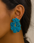 Close-up of a person wearing a blue floral earring against a neutral background