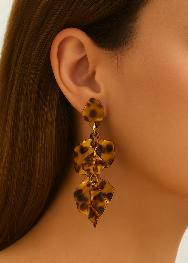 Close-up of a woman wearing tortoiseshell leaf-shaped earrings against a neutral background
