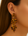 Close-up of a woman wearing tortoiseshell leaf-shaped earrings against a neutral background
