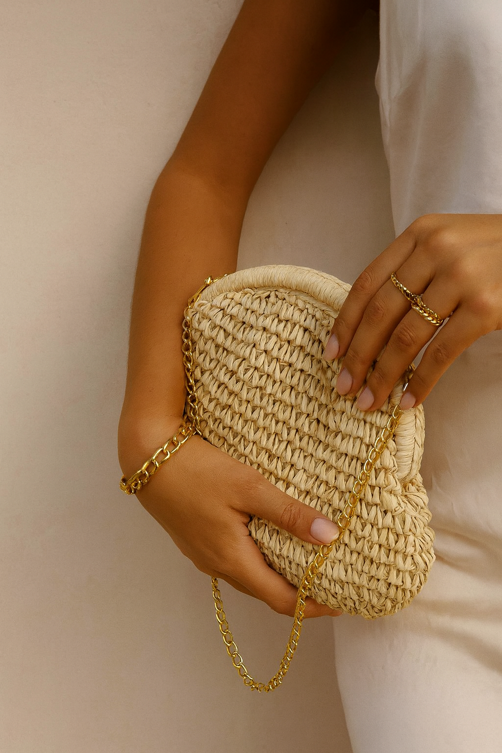 Person holding a woven clutch with a gold chain against a neutral background