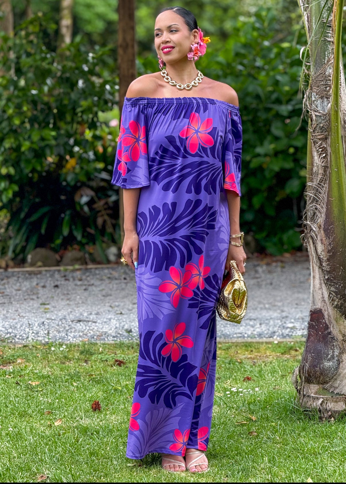 Woman wearing a purple floral dress standing outdoors with greenery in the background