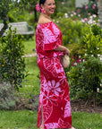 Woman in a red and pink floral dress standing in a garden.