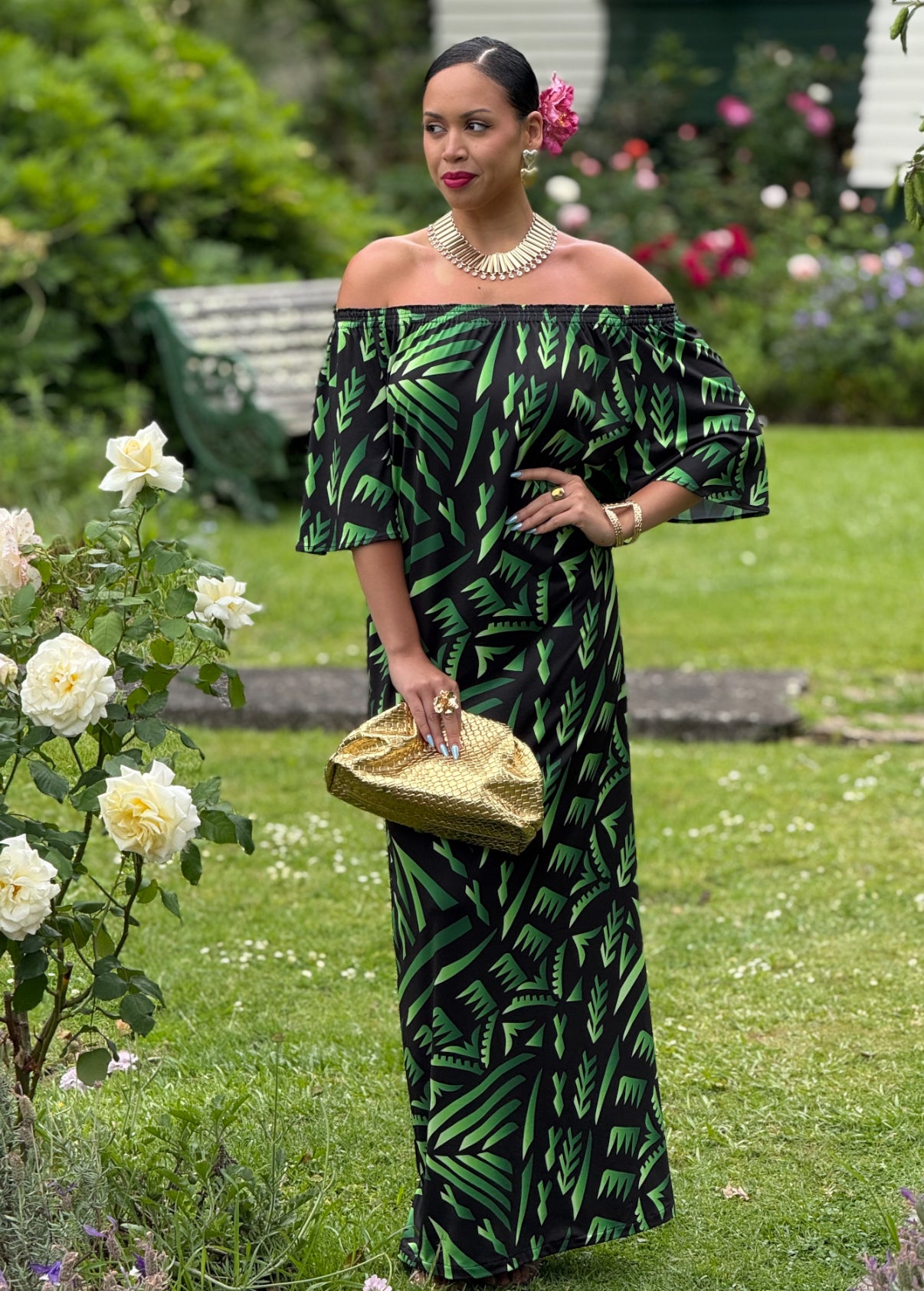 Woman in a green and black patterned dress standing in a garden with flowers.