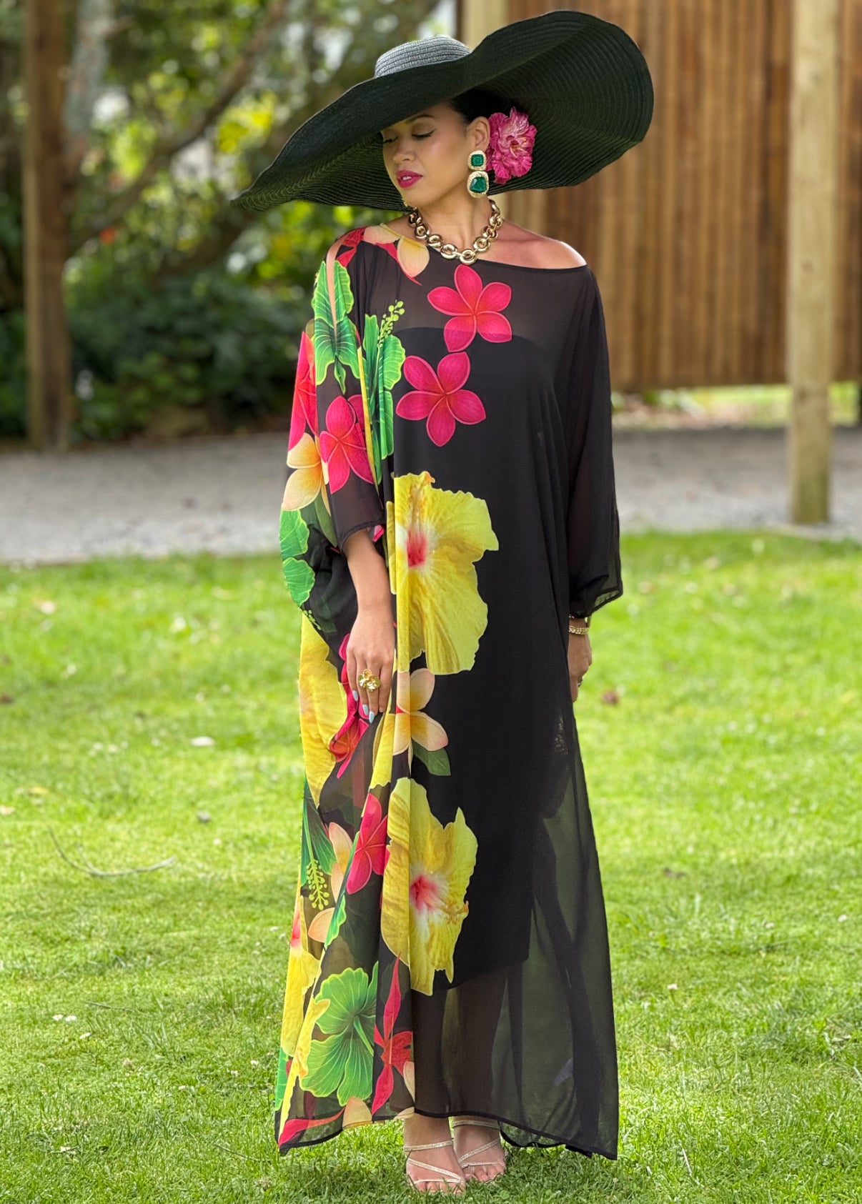 Woman in a black floral dress with colorful flowers standing on grass.