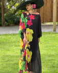 Woman in a black floral dress with colorful flowers standing on grass.
