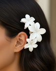 Woman with dark hair wearing a white floral hair accessory against a neutral background