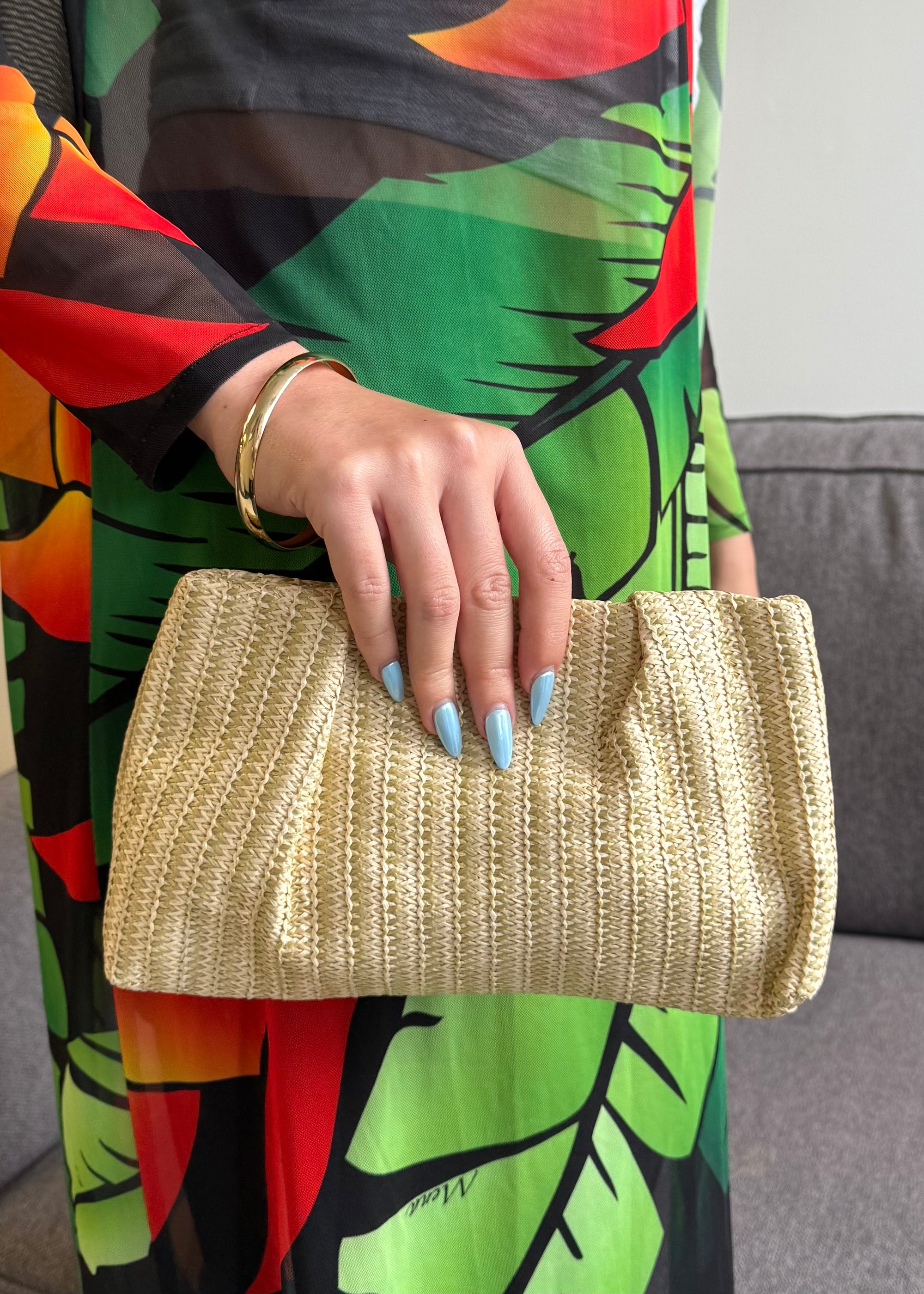 Person holding a beige clutch with a colorful dress in the background