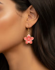 Close-up of a woman wearing pink flower earrings with a neutral background