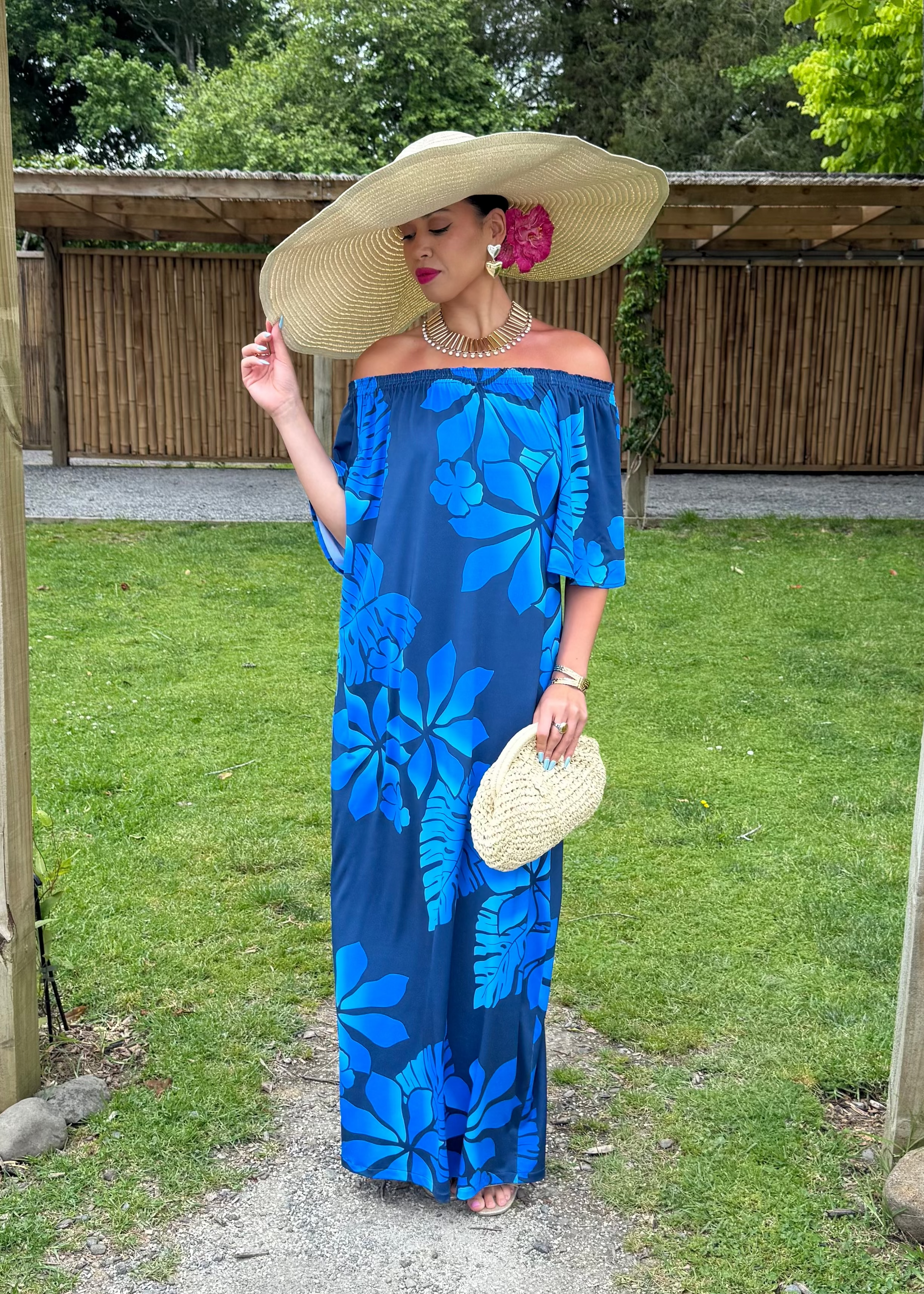 Woman in a blue floral dress standing under a wooden archway with greenery in the background