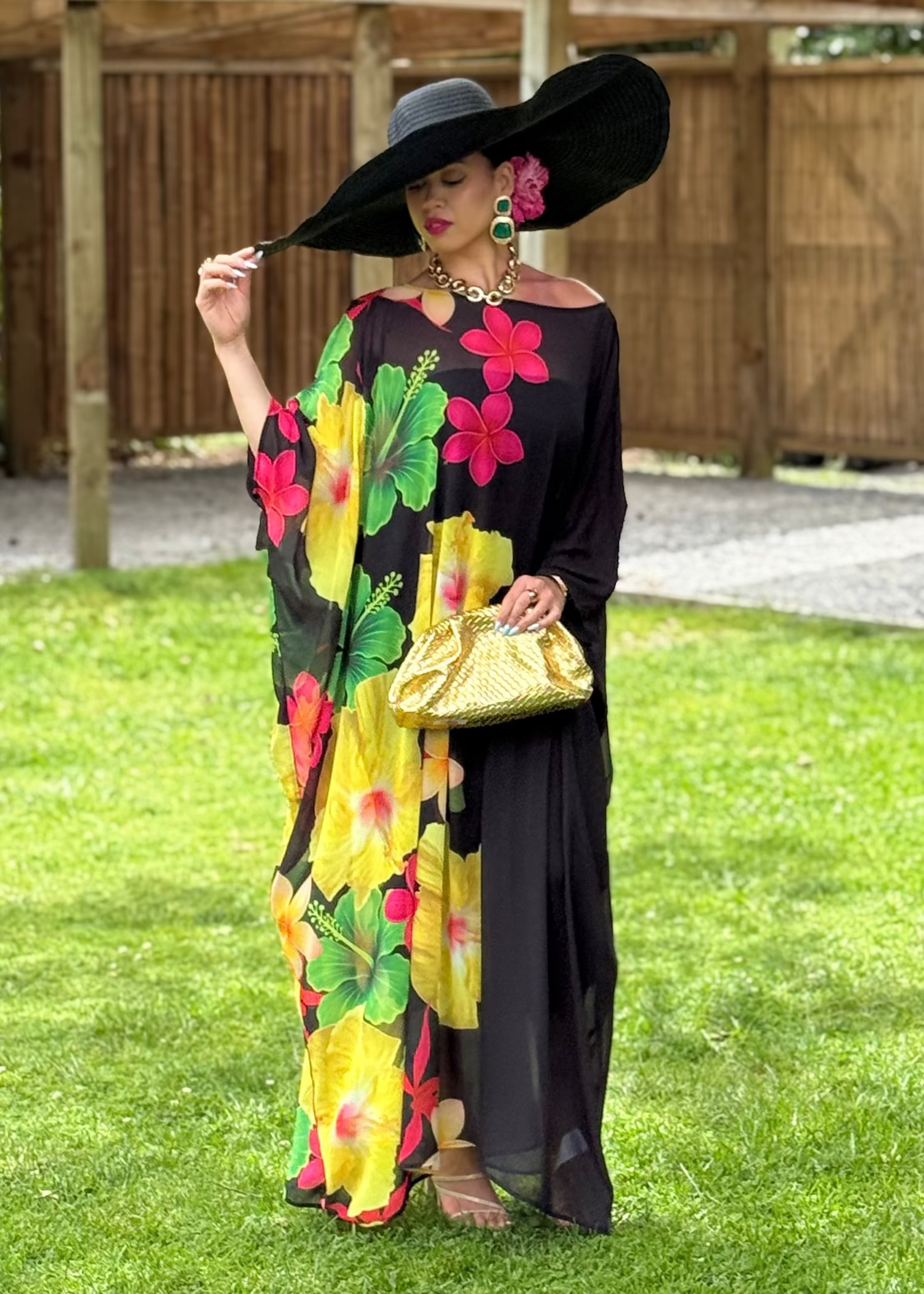 Woman in a colorful floral dress and black hat standing on grass