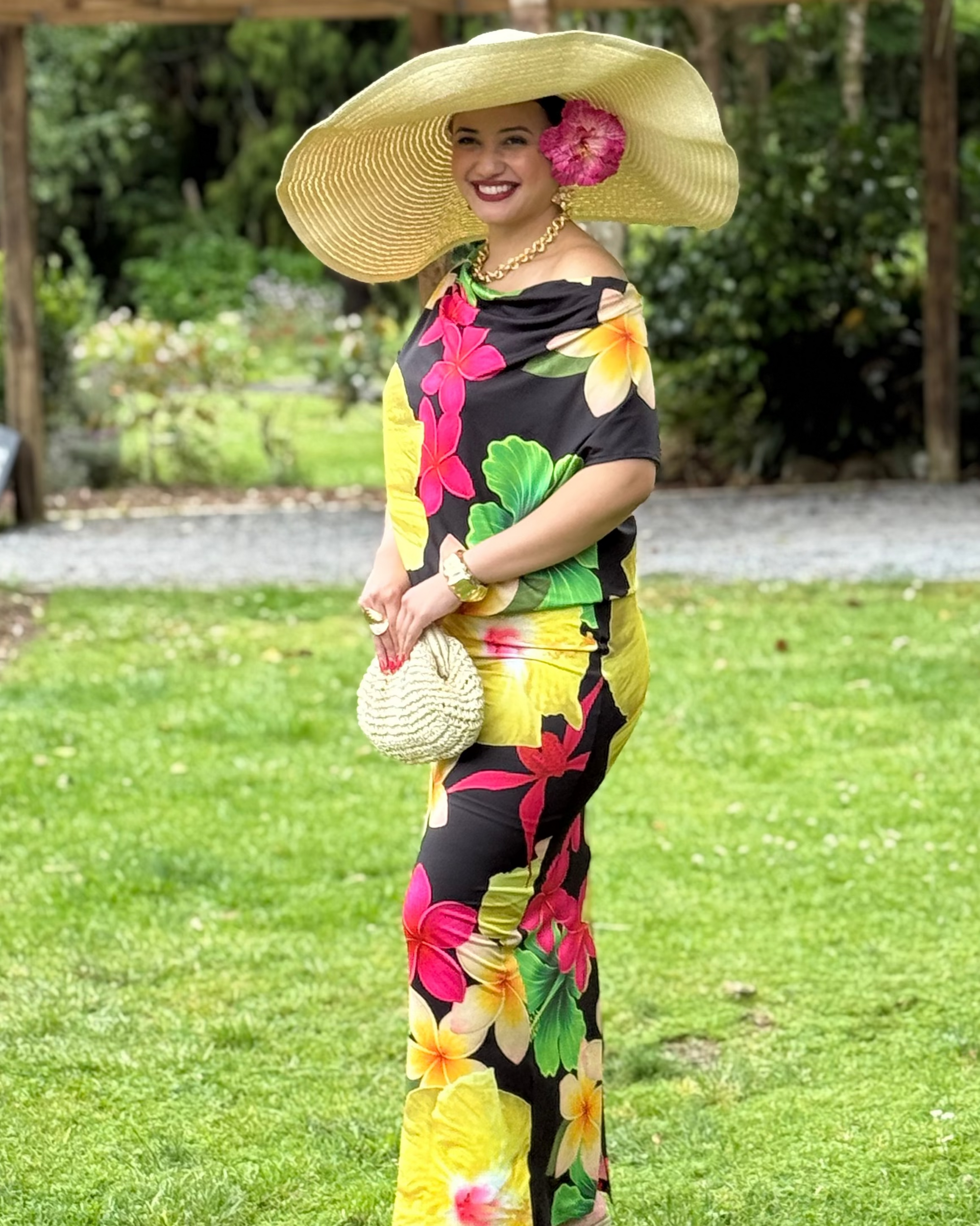 Woman in a colorful floral outfit with a large hat standing on grass.