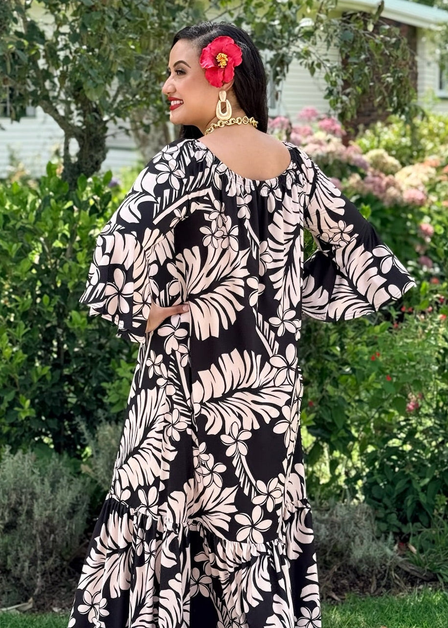 Woman in a black and white patterned dress standing outdoors with greenery in the background