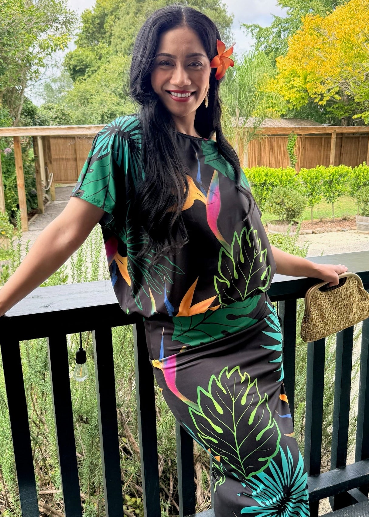 Woman in a colorful outfit standing on a balcony with greenery in the background