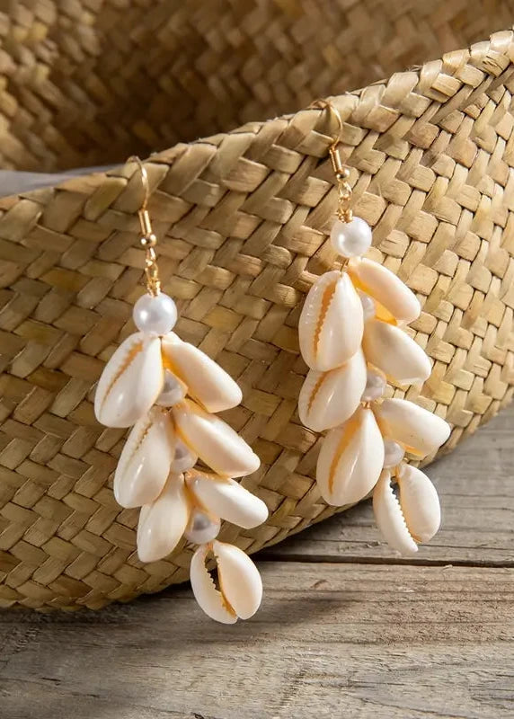 Shell and pearl earrings on a wooden surface with a woven basket in the background