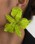 Close-up of a person wearing a bright green floral earring against a neutral background